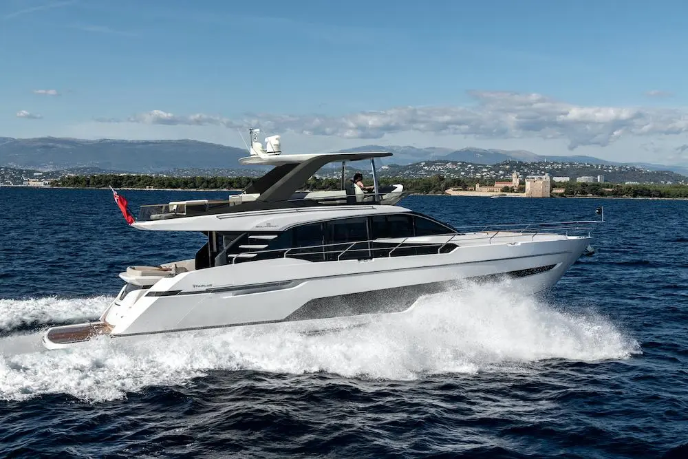 Elegant yacht cruising on blue water with mountains in the background and a visible castle on the shore.